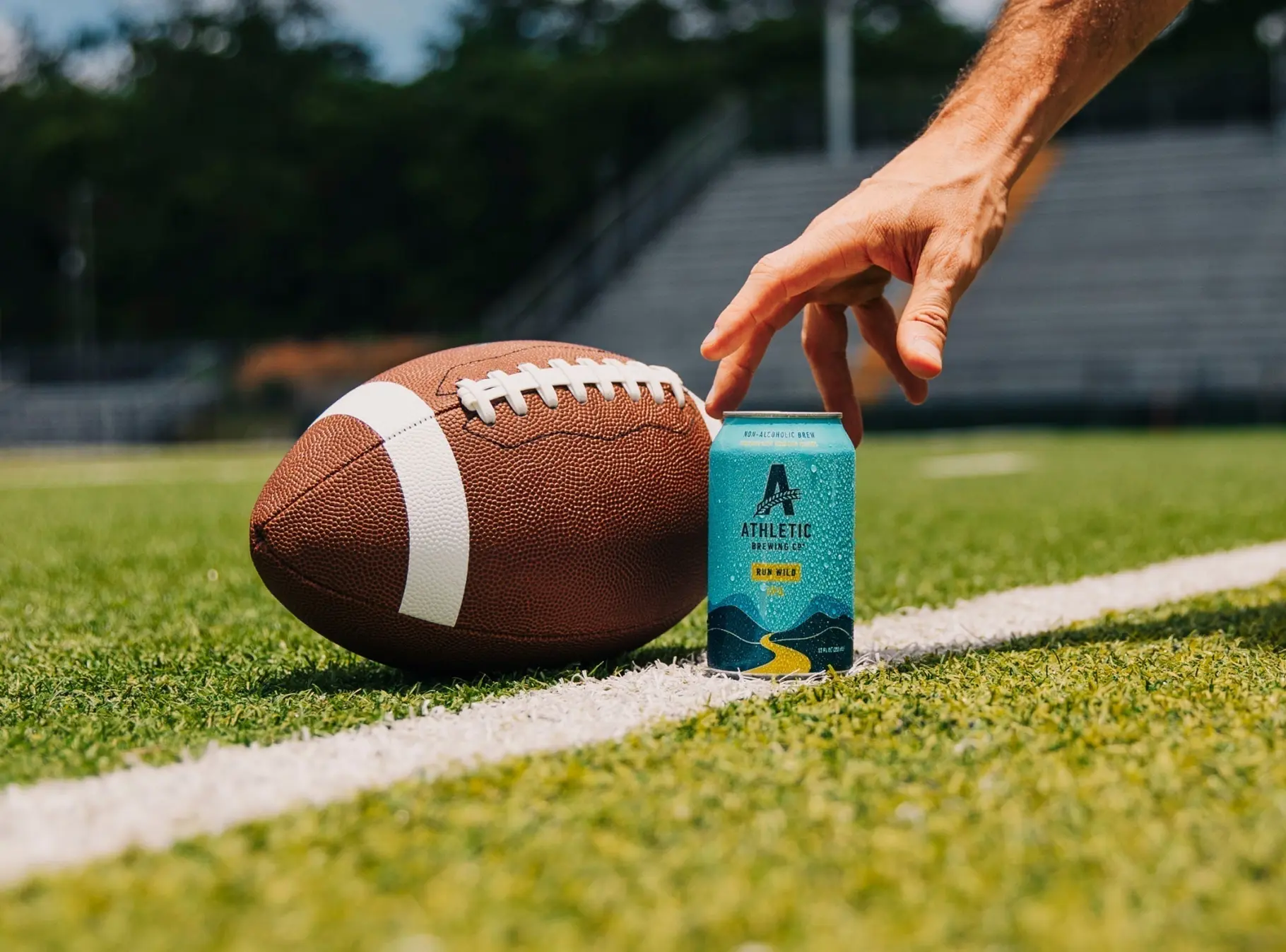 Cans of Athletic Brewing's Run Wild IPA and Upside Dawn Golden displayed in a football-themed promotional setting