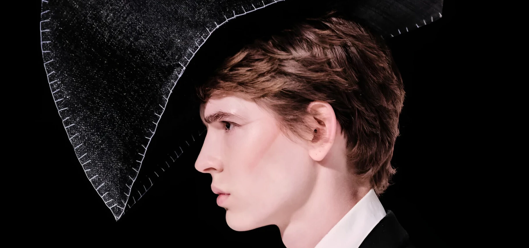 Model on the Mithridate SS27 runway wearing boxy tailoring loosened at the shoulder, staged in a club-style basement set.